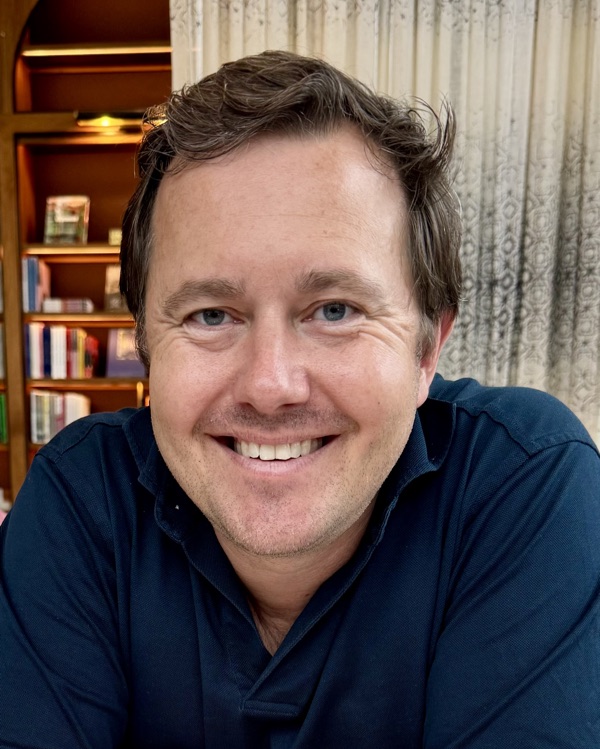 Alexander Oettl, in a navy polo shirt, in front of a bookshelf